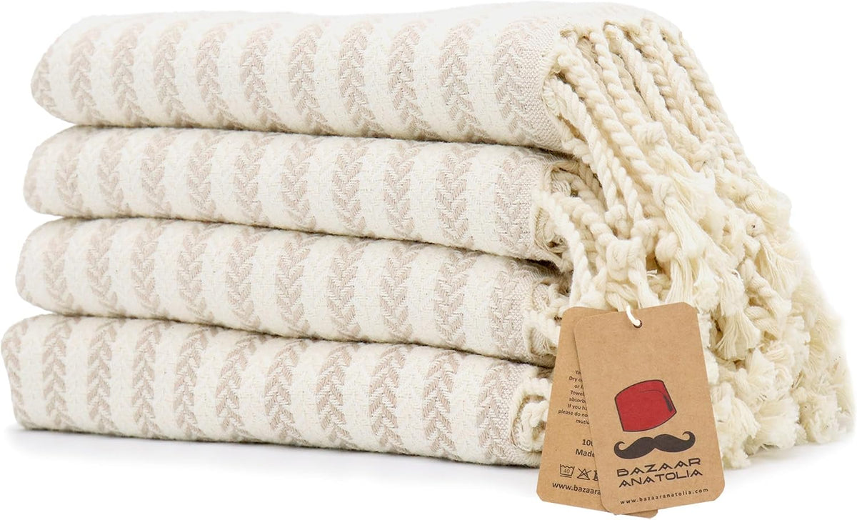 Set of four beige Arpa Turkish cotton hand towels with tasseled ends.