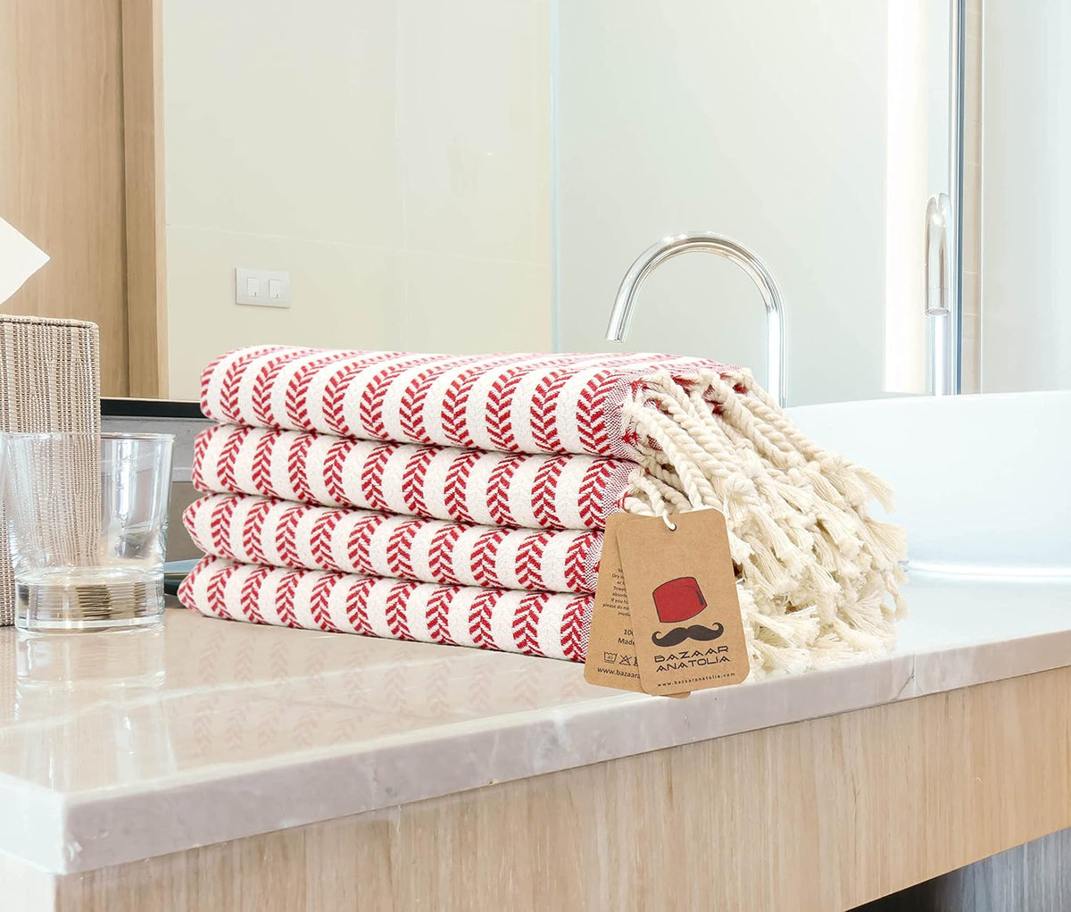 Set of four red Arpa Turkish hand towels folded beside a bathroom sink with cream tasseled ends.