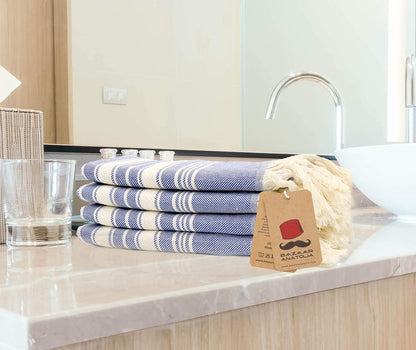 Four royal blue Stripe Turkish cotton hand towels stacked on a bathroom counter with cream tassels.