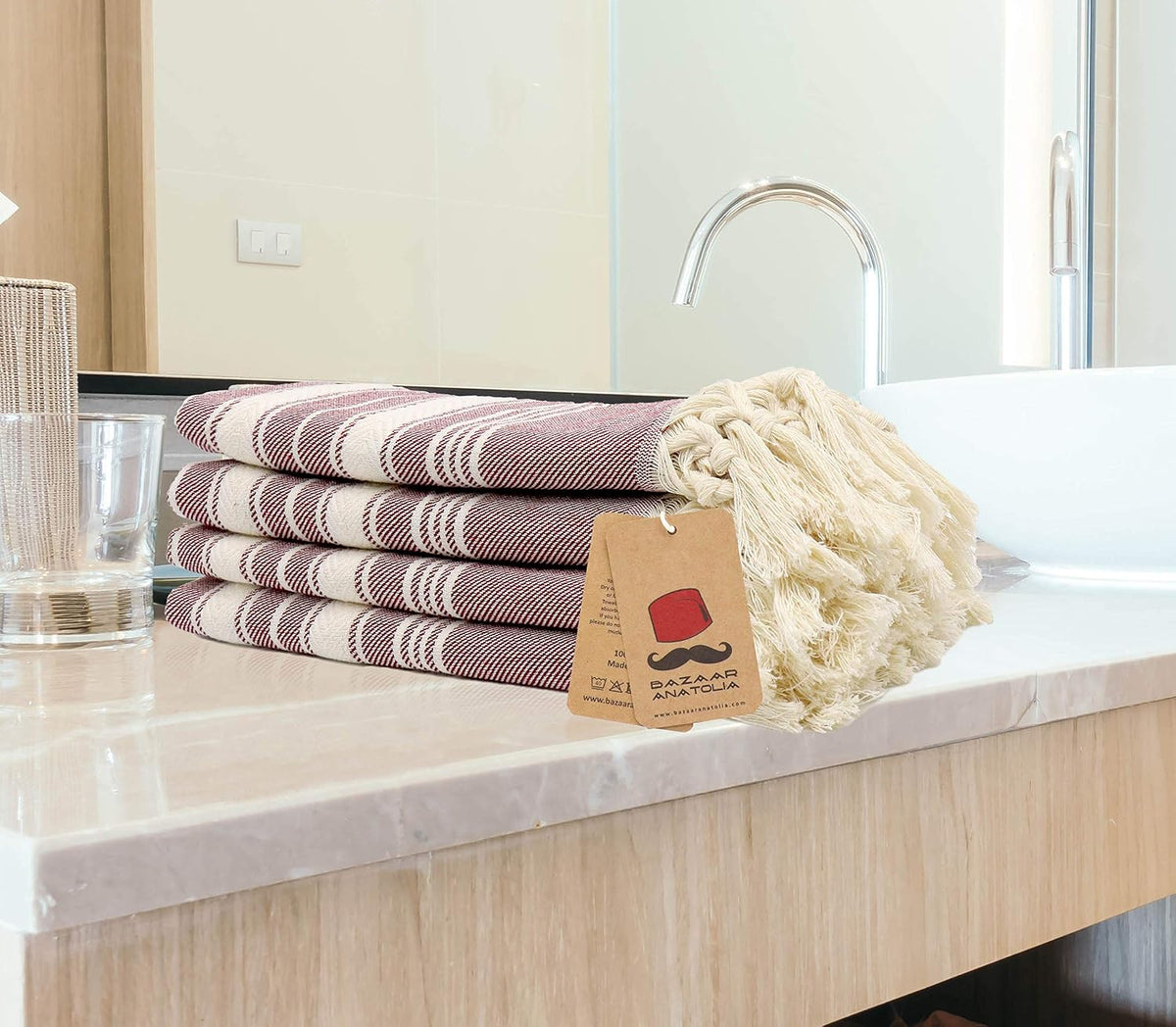 Four folded maroon Stripe Turkish hand towels stacked beside a bathroom basin with cream tasseled ends.