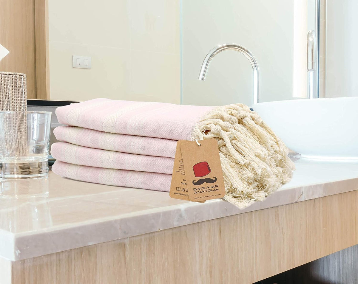 Four pink Stripe Turkish cotton hand towels folded beside a bathroom basin with cream tassels.