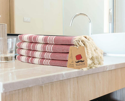 Four red Stripe cotton hand towels folded on a bathroom counter with cream tassels and a Bazaar Anatolia tag.