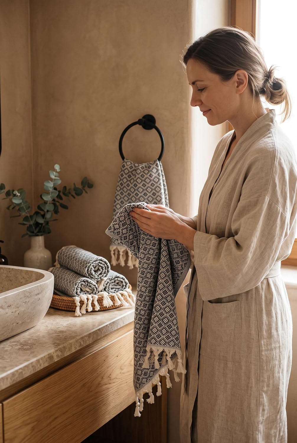 Woman holding a dark gray Ethnic Turkish hand towel beside a bathroom sink and matching rolled towels.