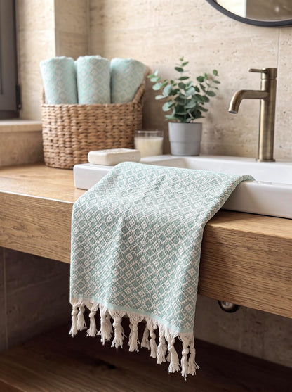 Mint Ethnic cotton hand towel draped beside a bathroom basin with matching rolled towels in a woven basket.