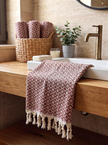 Maroon Ethnic hand towel draped over a bathroom basin with matching rolled towels in a woven basket.