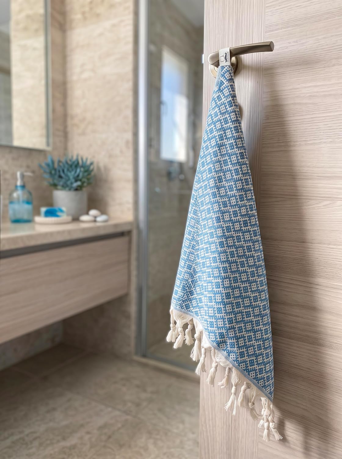 Turquoise Ethnic patterned cotton hand towel hanging from a bathroom hook, showing its cream tassels.