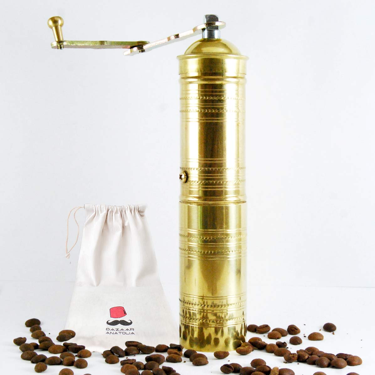 Handmade brass Turkish coffee grinder with a foldable crank handle, designed for fine coffee bean grinding, shown with Bazaar Anatolia branded storage pouch and coffee beans.